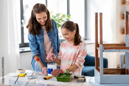 repair, diy and home improvement concept - happy smiling mother and daughter in protective gloves stirring grey color paint in can for painting old wooden table at home