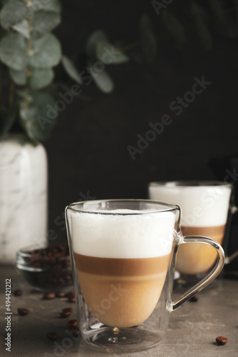 Glass cups of delicious latte macchiato and scattered coffee beans on grey table