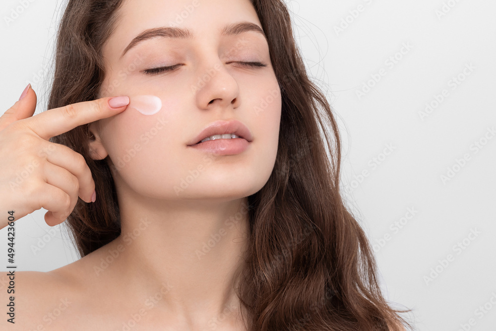 Portrait of young woman applying moisturizer cream on her face. Portrait of young woman applying moisturizer cream on her face.