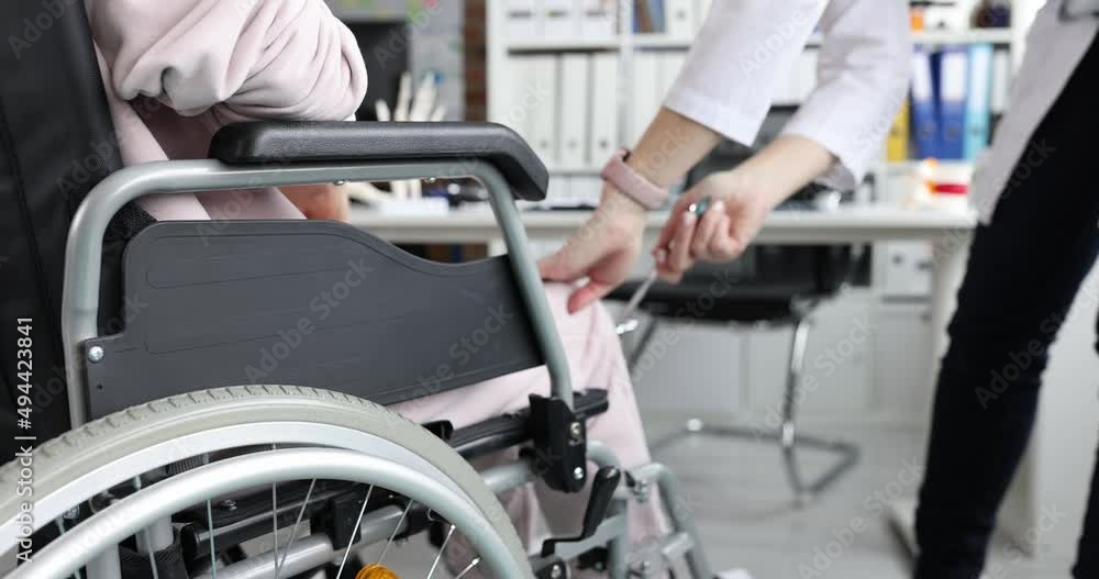 Doctor taps knee of patient in wheelchair with hammer Doctor taps knee of patient in wheelchair with hammer