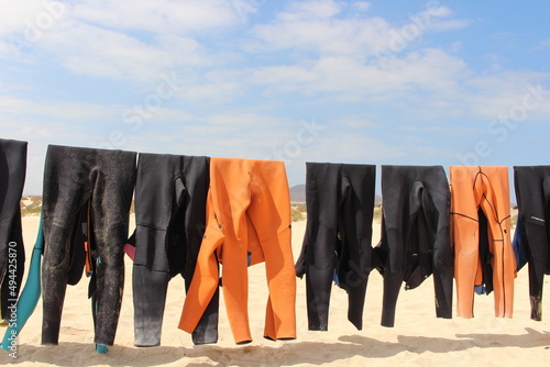 Colorful wetsuits hanging on a rope to dry in the sun at the beach  photo