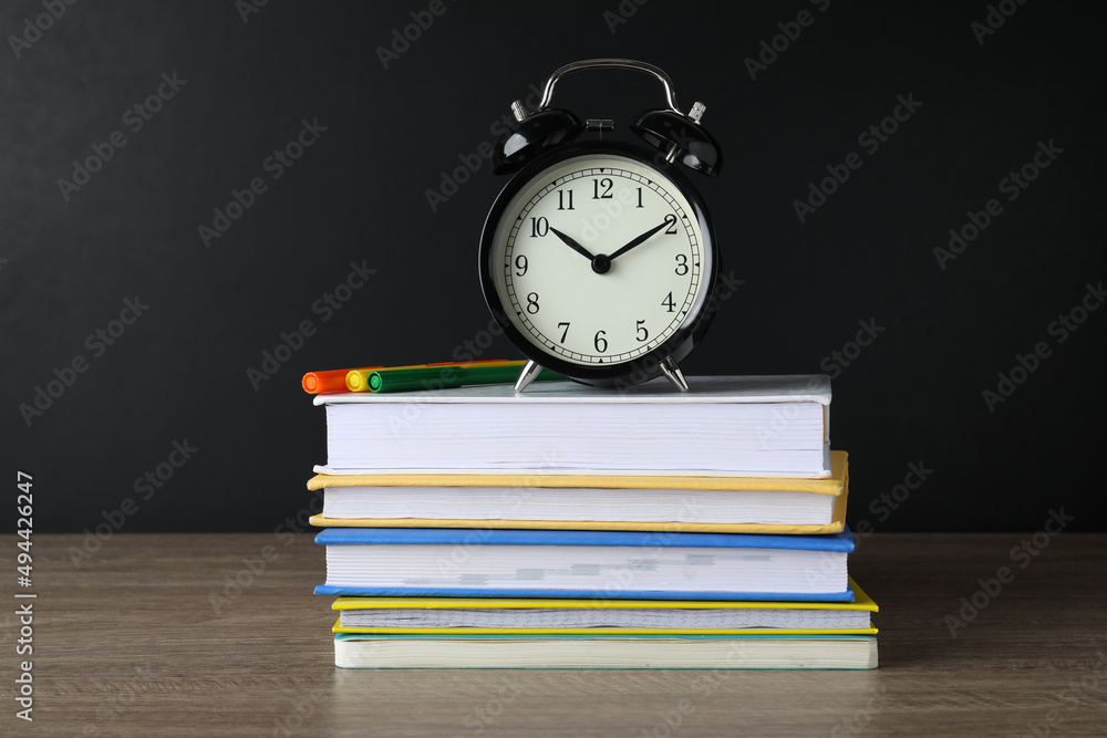 Alarm clock and stacked books on wooden table near blackboard. School time Alarm clock and stacked books on wooden table near blackboard. School time