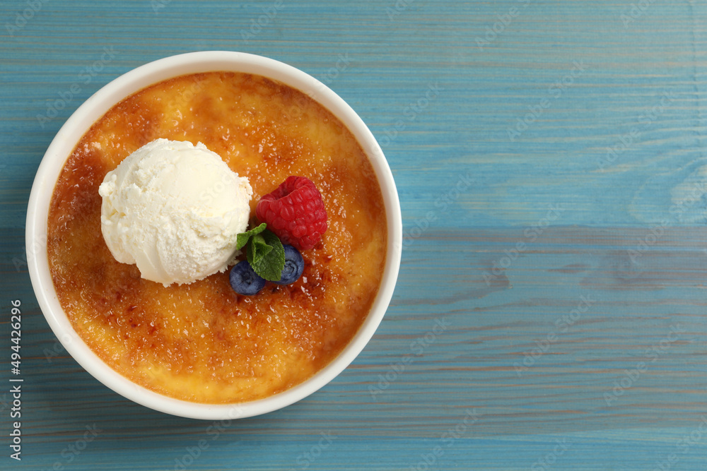Delicious creme brulee with scoop of ice cream, fresh berries and mint on light blue wooden table, top view. Space for text Delicious creme brulee with scoop of ice cream, fresh berries and mint on light blue wooden table, top view. Space for text