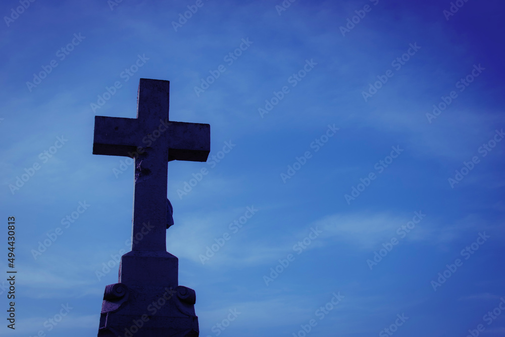 Dark stone cross on deep blue sky background