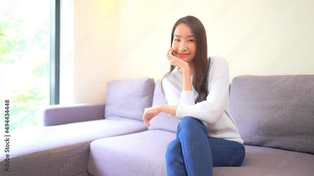 A young woman sitting on a couch places her chin in her hand and smiles. Title space A young woman sitting on a couch places her chin in her hand and smiles. Title space
