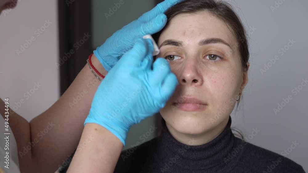 gloved hands wipe henna from dyed eyebrows with a cotton pad gloved hands wipe henna from dyed eyebrows with a cotton pad