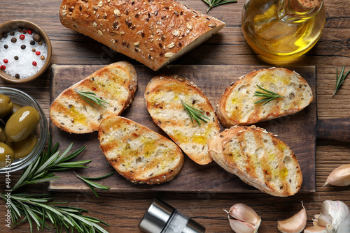 Tasty bruschettas with oil and rosemary on wooden table, flat lay photo