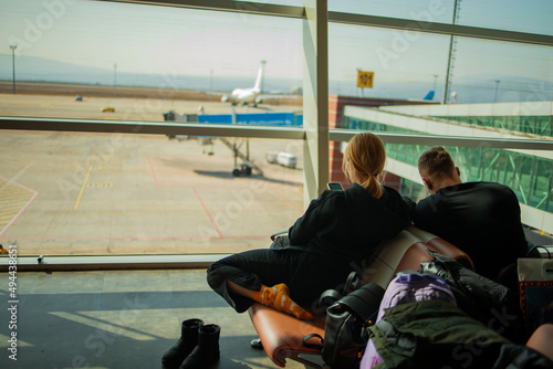  couple is waiting for a flight using smartphone in the airport terminal. They are wearing protective masks to prevent infection with coronavirus.