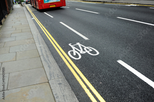 Cycle lane with bicycle symbol on the streets of London, UK and red bus. Ecological and sustainable transport. Energy saving. White bike icon on black asphalt texture. Urban scene