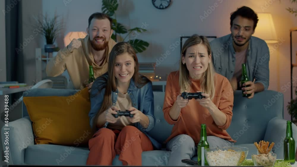 Portrait of carefree youth playing video game and doing high-five having fun in dark apartment at night. Friends drinking beer and clinking bottles celebrating victory. Portrait of carefree youth playing video game and doing high-five having fun in dark apartment at night. Friends drinking beer and clinking bottles celebrating victory.