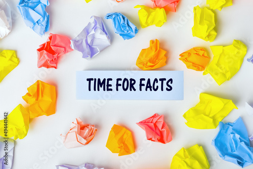 Blue sticky note with the text TIME FOR FACTS and some colorful crumpled paper balls around it on white background. Still life, Flat lay design, View from above