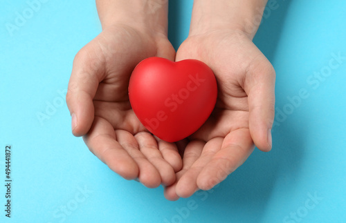Fototapeta Naklejka Na Ścianę i Meble -  Man holding red decorative heart on light blue background, top view. Cardiology concept