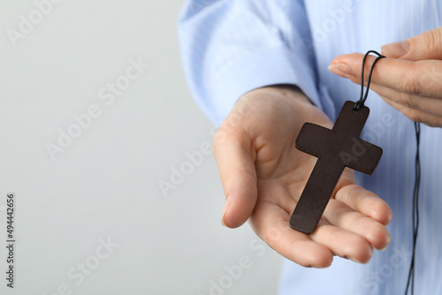 Woman holding wooden Christian cross on light grey background, closeup. Space for text