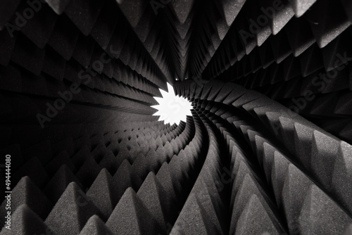 Roll of dark gray triangular acoustic foam rubber and light hole. The pattern of the soundproof panel of polyurethane foam. Shockproof foam. Selective focus.	 photo