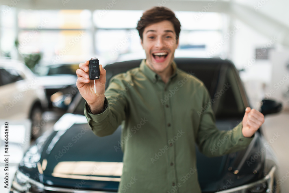 Excited young Caucasian man showing new car key at camera, gesturing YES, celebrating purchase of auto at dealership Excited young Caucasian man showing new car key at camera, gesturing YES, celebrating purchase of auto at dealership