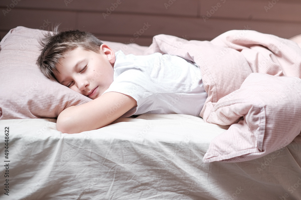 Boy teen sleeping on the bed in morning. Beds blanket is in light pink colors Boy teen sleeping on the bed in morning. Beds blanket is in light pink colors