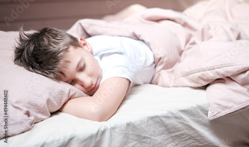 Boy teen sleeping on the bed in morning. Beds blanket is in light pink colors
