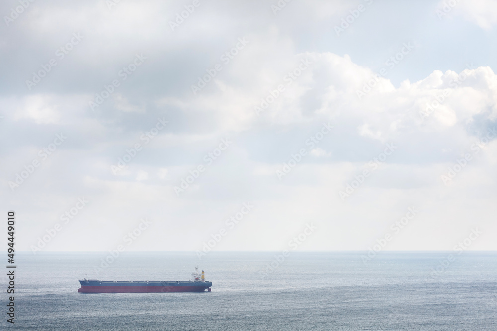 A big cargo ship in the sea or ocean floats on the waves against the background of a large sky. A big cargo ship in the sea or ocean floats on the waves against the background of a large sky.