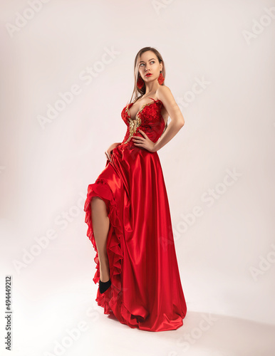 a beautiful girl in a red long dress poses on a white background