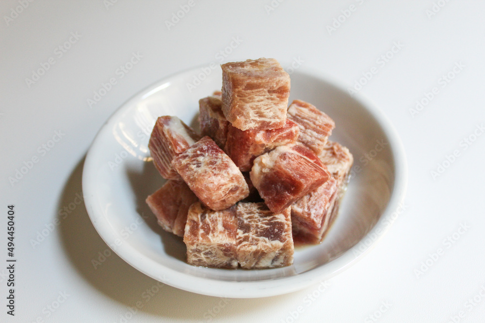 Uncooked diced beef, on a white small plate, isolated on white background