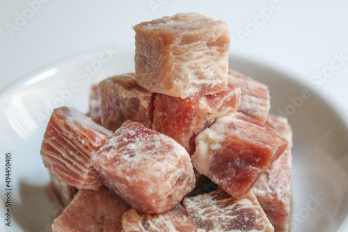 Uncooked diced beef, on a white small plate, isolated on white background