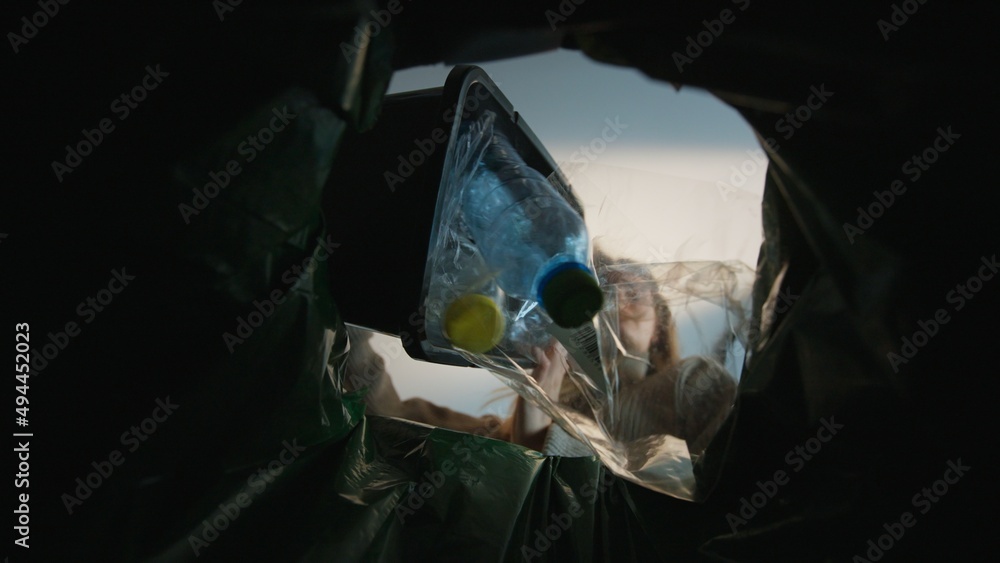 Woman throws a garbage bag in the trash. Bottom view from the trash bin. Ecology concept. Recycling