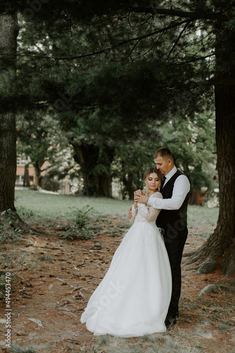 Happy handsome groom and brunette beautiful bride in white dress hugging under