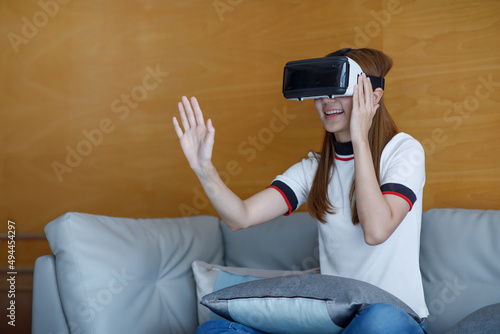 Young excited redhead woman testing VR glasses or goggles while sitting on armchair at home, working remotely. Impressed female with opened mouth using VR technology for the first time, gesturing