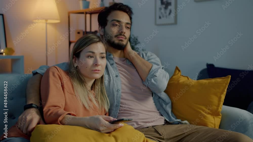 Sleepy young couple watching TV talking and hugging in the evening in apartment. Leisure activity and romantic relationship concept. Sleepy young couple watching TV talking and hugging in the evening in apartment. Leisure activity and romantic relationship concept.