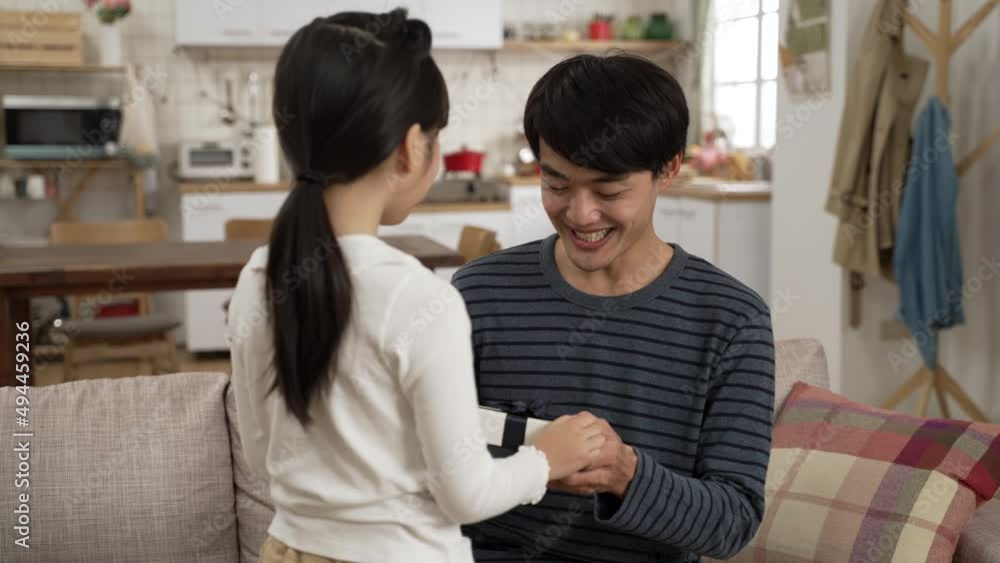 view from behind Asian little girl walking up to her dad and showing him a surprise gift in living room at home. happy father embracing her daughter for the sweet act on father's day view from behind Asian little girl walking up to her dad and showing him a surprise gift in living room at home. happy father embracing her daughter for the sweet act on father's day