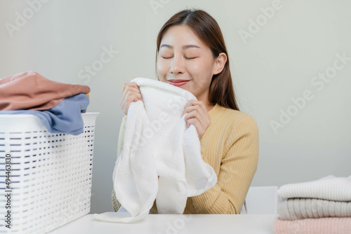 Feel softness, smiling asian young woman, girl touching fluffy towel cotton, smelling fresh clean clothes on table after washing, laundry, dry. Household working at home. Laundry and maid.