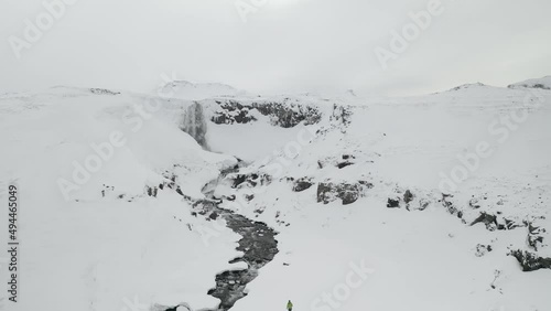 Man Walking Towards Icy Waterfall In Iceland On Winter - aerial shot photo