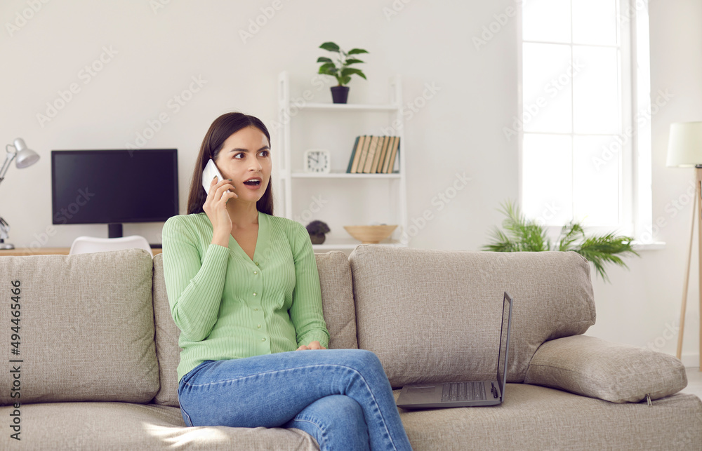Young girl sharing news and learning latest gossip on phone. Beautiful Caucasian woman sitting on sofa at home and talking to her friend on cellular phone with surprised, shocked face expression Young girl sharing news and learning latest gossip on phone. Beautiful Caucasian woman sitting on sofa at home and talking to her friend on cellular phone with surprised, shocked face expression