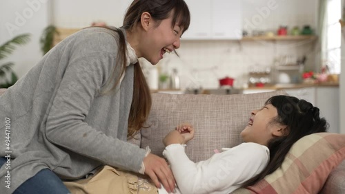 slow motion of Asian mother and daughter having fun playing tickle together on living room couch at home. the girl pushes her mom away while laughing with excitement