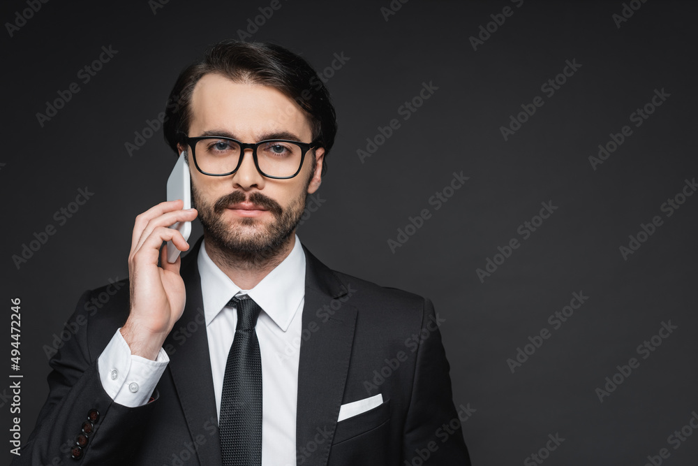 businessman with mustache talking on smartphone on dark grey. businessman with mustache talking on smartphone on dark grey.