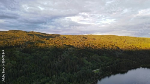 Soft sunlight spreading over the forest and valleys around Dease Lake in British Columbia, Canada. Wide angle aerial panning shot at sunset photo