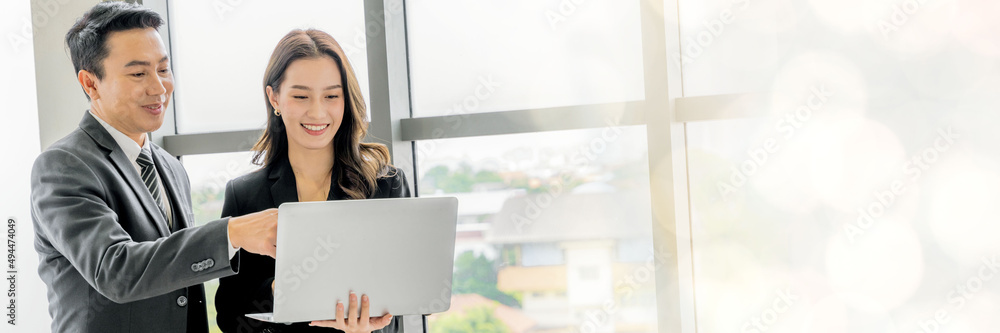 An Asian business executive inspects the work of a female employee at her laptop. Talk with smiling faces and have fun and relax. at the office of the company web banner with copy space on right An Asian business executive inspects the work of a female employee at her laptop. Talk with smiling faces and have fun and relax. at the office of the company web banner with copy space on right