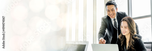 An Asian business executive inspects the work of a female employee at her laptop. Talk with smiling faces and have fun and relax. at the office of the company web banner with copy space on left