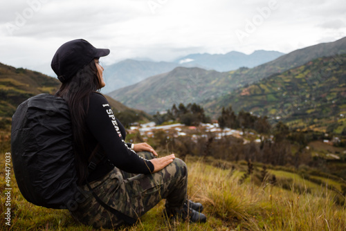 Hermosa foto de una feliz viajera hispana con una mochila sentada en la cima de montañas verdes