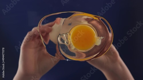 Breaking and spilling egg onto glass surface. Bottom up view. Female hands holding a cracked egg. Breaking an egg seen from the frying pan. Slow motion. Camera pointing up.