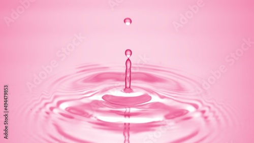 Macro shot of water drop falls down on pink transparent fluid surface creating water rings on it on pale pink background | Abstract skin moisturizing cosmetics formulation concept