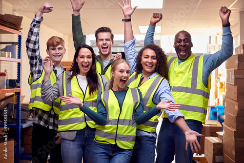 Portrait Of Cheering Multi-Cultural Team Wearing Hi-Vis Safety Clothing Working In Modern Warehouse photo