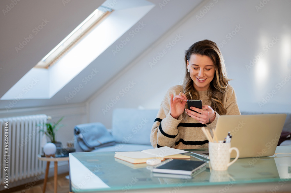 Woman using smartphone while working at home and using a laptop Woman using smartphone while working at home and using a laptop