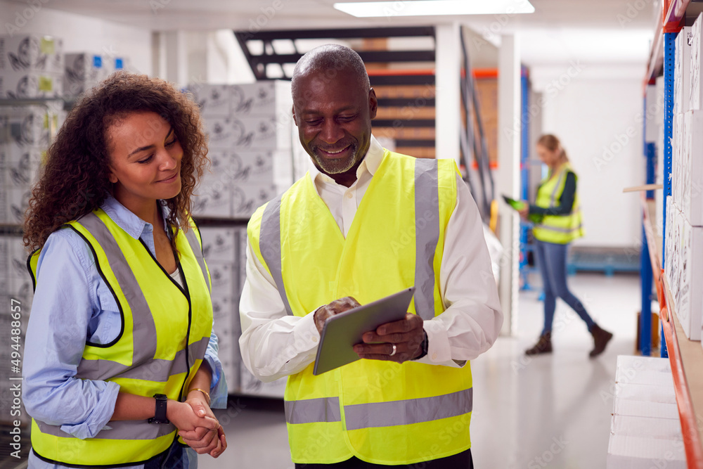 Male Team Leader With Digital Tablet In Warehouse Training Intern Standing By Shelves Male Team Leader With Digital Tablet In Warehouse Training Intern Standing By Shelves