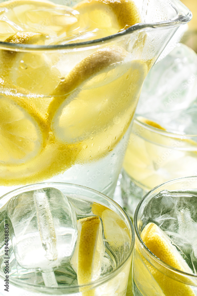 Frozen glass pitcher with lemonade with ice and pieces of lemon surrounded by glasses of water with lemon. Refreshing summer drink concept for hot days Frozen glass pitcher with lemonade with ice and pieces of lemon surrounded by glasses of water with lemon. Refreshing summer drink concept for hot days