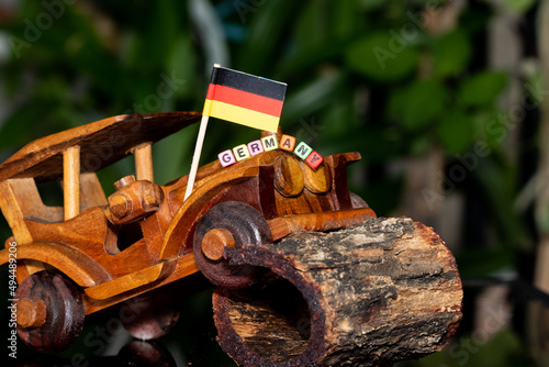 Mote alphabet blocks arranged into "Germany" on a miniature wooden car on the background of the national flag.