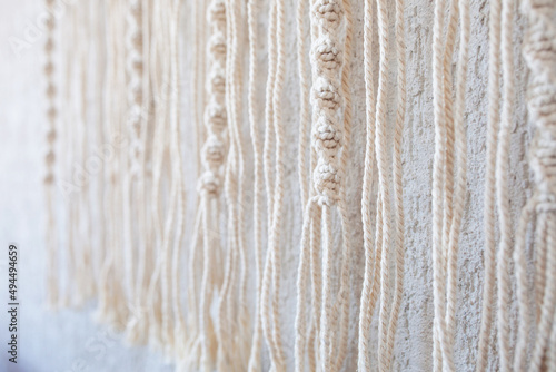 Handmade macrame wallhanging. 100% cotton wall decoration with wooden stick hanging on a white wall. Macrame braiding and cotton threads. Female hobby. ECO friendly modern concept in the interior