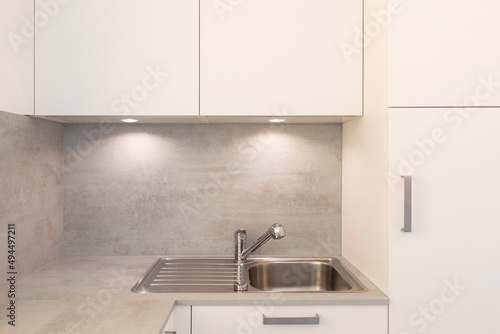Kitchen detail, stainless steel sink with white wall units and spotlights