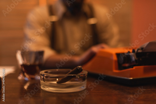 ashtray with cigar near typewriter machine and blurred man on background.