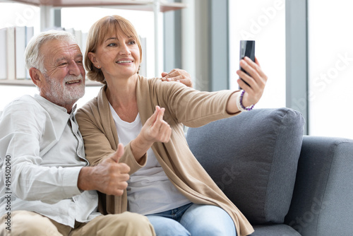 senior couple video call to someone or selfie from smartphone on sofa © offsuperphoto